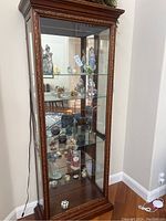 Full view of glass display cabinet with four shelves containing porcelain figurines, tea sets and other collectibles