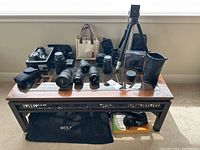 Wide overview of coffee table displaying all lenses, camera body, tripod and bags