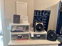 Full view of three clear plastic drawers with contents, Waterford and Atmio boxes on top, two small fans on adjacent drawer