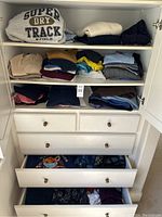 White cabinet with multiple shelves and drawers containing neatly folded sweaters, shirts, and pants in various colors including grey, beige, navy, yellow, and burgundy.