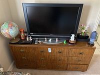 Front view of a Sony flat screen TV on top of a Drexel wood dresser with various small decorative items including figurines and a globe around it.