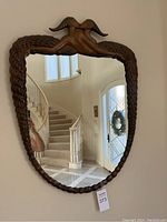 Full view of bronze Erte mirror hanging on wall in foyer, showing entire frame and glass.