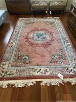 Full view of dusty rose floral area rug on hardwood floor with tassel fringe