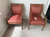Pair of ornate wood accent chairs side by side against white wall on carpeted floor