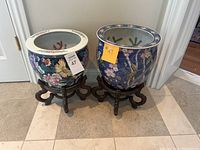 Front view of two round porcelain planter bowls with carved wooden stands