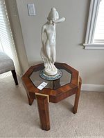 Full view of the octagonal wooden side table with glass top and the white porcelain statue placed on it.