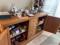 Top of cabinet showing porcelain teapot, sugar bowl, creamer, wooden mug, silver urn