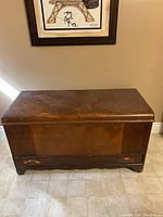 Front view of antique cedar chest showing wood paneling and rounded drawer handles on base.