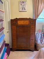 Front view of the antique high boy dresser showing the wood grain, inlay on top drawer, and brass handles.