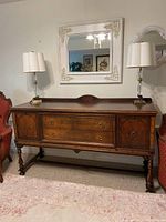 Front view of wooden sideboard showing two drawers, two cabinets, decorative veneer and turned legs