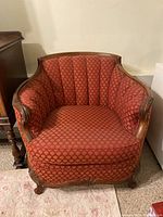 Front view of antique upholstered armchair with red fabric and carved wood frame.