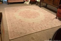 Full view of the pink and cream area carpet placed in a room with adjacent furniture, showing the central floral medallion and overall condition.