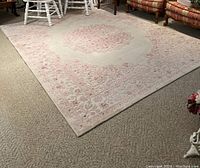 Top-down view showing full carpet with floral border and central medallion in pink on cream background.