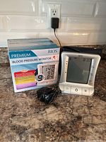 Photo of BIOS Premium Blood Pressure Monitor with box, power adapter, and cuff on kitchen counter.