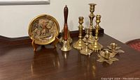Photo showing five brass candle holders and two hand bells along with the collector plate on a wooden surface.