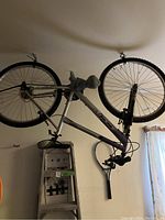 Side view of CCM bicycle hanging upside down in garage showing silver frame with purple accents, black saddle, and knobby tires