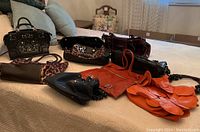 Photo showing entire assortment of nine handbags and purses displayed on bed, depicting variety of colors and styles including black, orange, leopard print and burgundy handbags