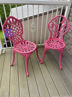 Pair of pink iron garden chairs with intricate floral backs and seats on a porch deck