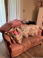 Photo showing six pillows with floral and Paris designs placed on pink upholstered sofa, plus two throws
