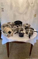 Full view of all pots, pans, lids, roasting pan, colanders and enamelware pot arranged on table
