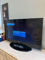 Front view of Samsung TV powered on showing message on screen, with remote placed on the base stand.