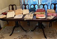 Wide view of dining table with various folded table cloths and napkins in multiple colors and patterns, neatly arranged.