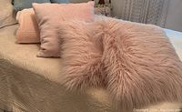 Three pink throw pillows arranged on a bed, showing different textures: smooth, textured, and furry.