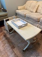 Full view of the white painted vintage coffee table with serving tray and magazine rack next to seating.