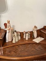 Collection of 12 Willow Tree Guardian Soul figurines arranged on a wooden surface including an angel, multiple children, two adults embracing, and a nativity figure.