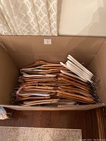 Box filled with a mix of natural wood and white wooden coat hangers with metal hooks, viewed from above.