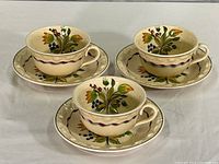 Set of three Adams Titian Ware hand-painted cups and matching saucers arranged on a white surface, showing floral designs and condition.