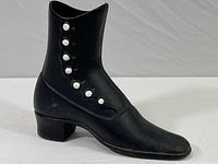 Life-size black cast iron button-up shoe sculpture showing overall side profile with button details and block heel.