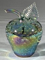 Full view of the iridescent crystal apple sculpture showing its shape, bubble inclusions, and color sheen.