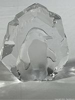 Clear glass block paperweight with sculpted penguin inside, shown from one side.