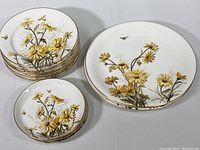 Stack of smaller plates and saucers showing yellow daisy floral design, bees, and gold rims