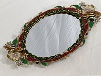 Full view of the oval mirrored tray showing the scalloped enameled metal frame with floral and bee decorations.