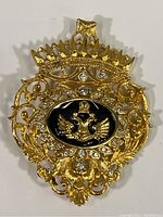 Full view of the gold tone brooch with double headed eagle, rhinestones, and ornamental design