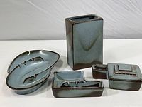 Photo of four blue-gray glazed Frankoma pottery pieces: two ashtrays, one rectangular vase, one covered dish with match holder, showing all items together.