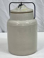 Front view of cream-colored vintage stoneware jar with wire lid closure, showing smooth finish and cylindrical shape.