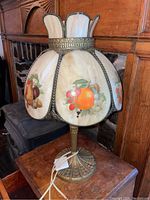Full view of the lamp showing curved painted glass panels with fruit designs and heavy solid brass base.
