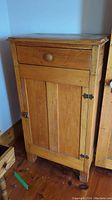 Front view of small wooden cabinet with top drawer and bottom door, wood grain visible
