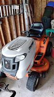 Side view of orange Columbia riding mower showing seat, steering wheel, front grill and deck
