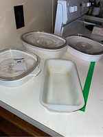 Three white baking dishes on countertop, two with clear glass lids, one long meatloaf dish with green spice pattern along side