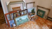 Photo of assorted vintage frames and artwork arranged on carpet. Includes large and small frames with landscape paintings.