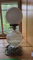 Full view of the lamp showing cut glass base, metal stand, and frosted glass globe shade.