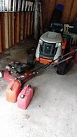 Photo of Yard Machine push lawn mower with 20 inch cut deck, Tecumseh motor, accompanied by two fuel cans (one large orange and one smaller red) placed in front.