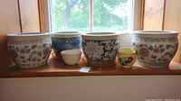 Front-facing view of five ceramic plant pots with various floral and geometric patterns placed in window ledge light.