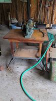 Full view of Delta scroll saw mounted on wooden table in a garage with other tools visible in background.