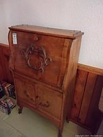 Full view of vintage wooden secretary desk showing its carved drop-front, two-door storage cabinet below, and brass gallery rail on top.