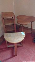 Three wooden tables grouped: a plant stand, clover leaf shaped table, and half moon shaped table on red carpeted floor near wall corner.